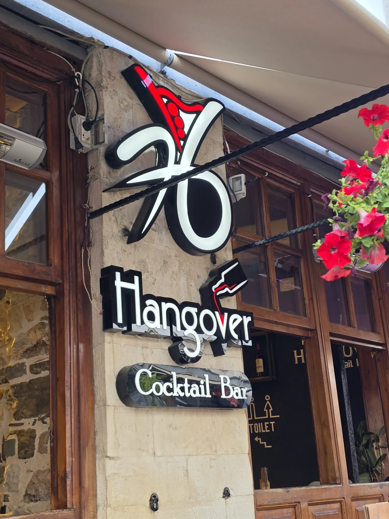 The Hangover Cocktail Bar sign above the door on Rruga Ismail Kadare, with red geraniums