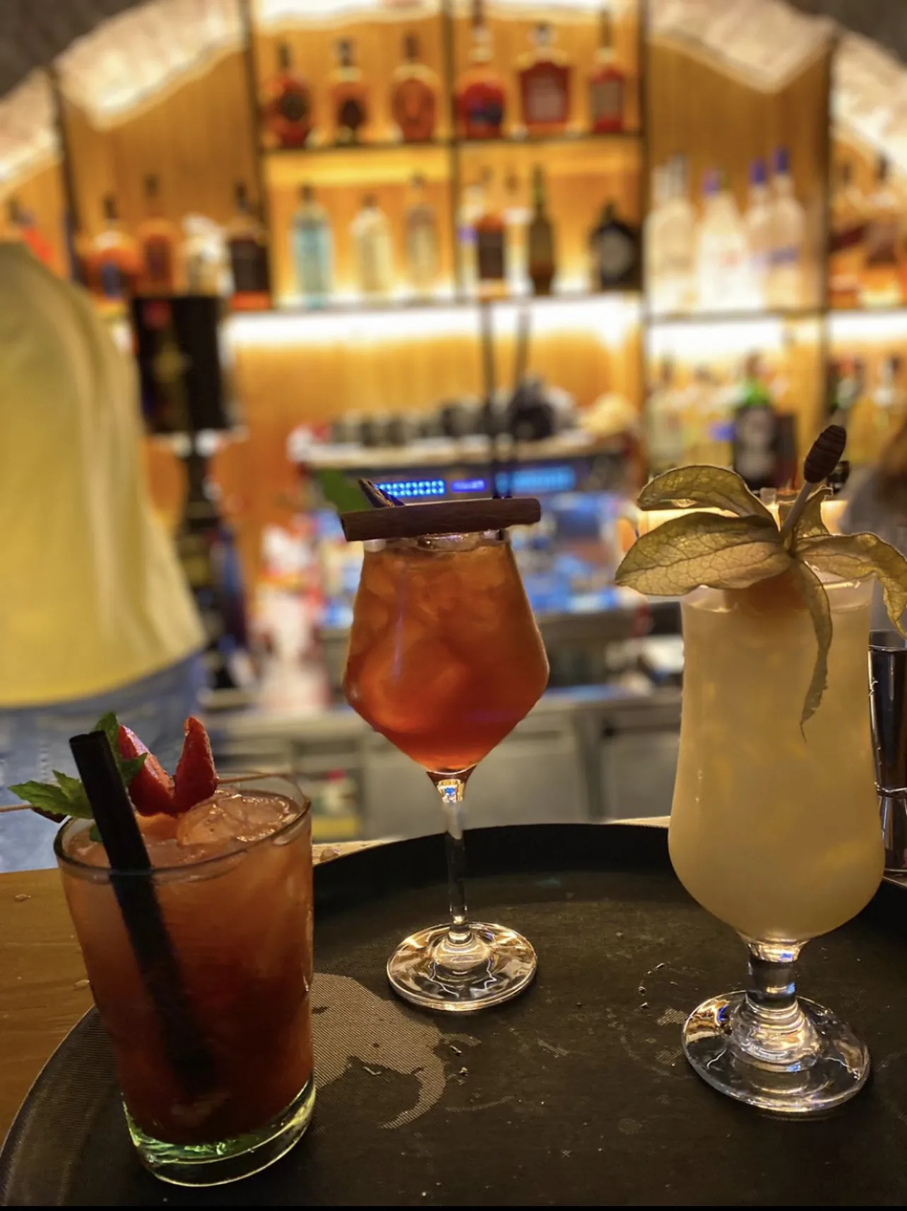 Three Hangover cocktails on a tray in front of the lit back bar