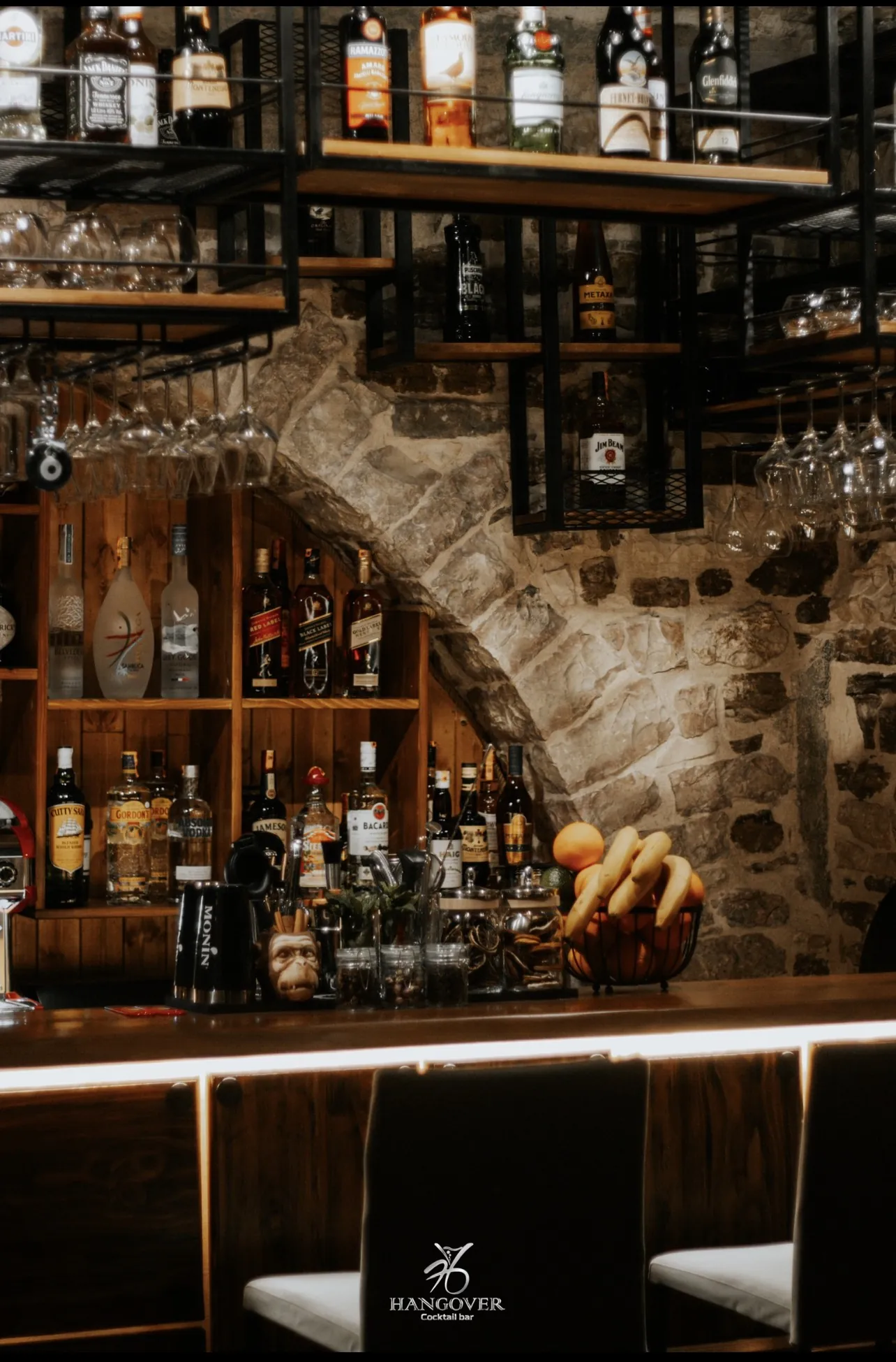 The Hangover back bar with bottles, hanging glasses and a stone arch