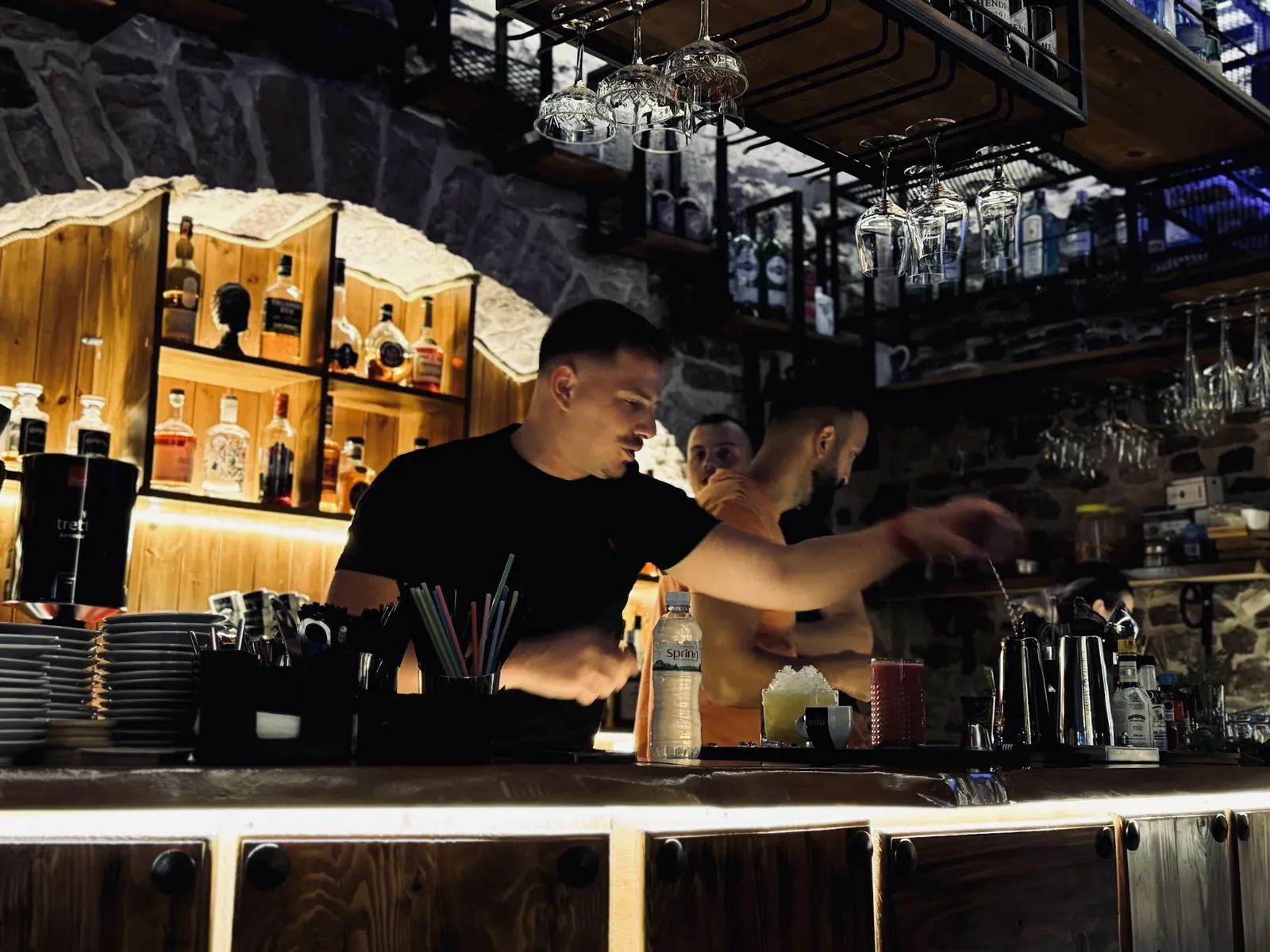 A Hangover bartender pouring a cocktail under the stone arch of the back bar